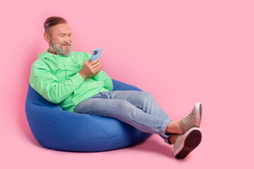 Full size photo of cool pensioner man sit bean bag eshopping hold device wear trendy green clothes...