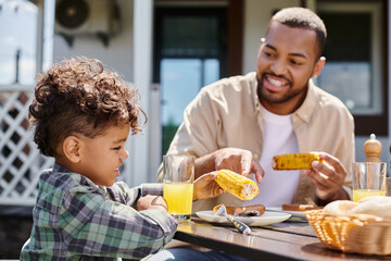 Fototapeta na wymiar positive african american kid having family bbq with father on backyard of house, orange juice