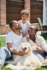 quality time of happy african american parents and son smiling and sitting on grass near dog