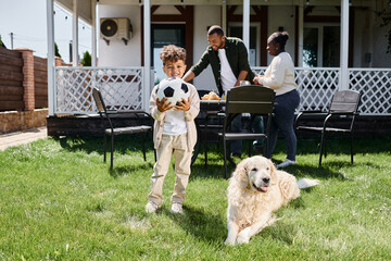family time, happy african american boy holding football near parents and dog on backyard of house