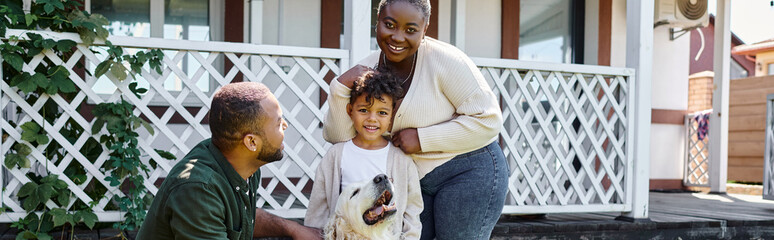 family banner, cheerful african american parents and son smiling near cute dog on backyard of house
