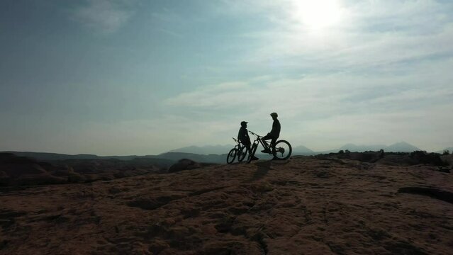 Mountain bike, silhouette and sports people relax during outdoor ride, desert journey or off road cycling. Sky, adventure and dark shadow of athlete on break after bicycle training with partner