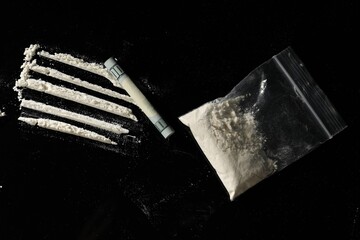 Drug addiction. Plastic bag with cocaine and rolled dollar banknote on black background,, flat lay