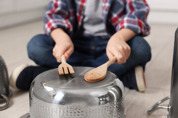 Little boy pretending to play drum on pot indoors, closeup