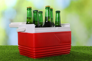Plastic cool box with glasses of drink on artificial grass, closeup