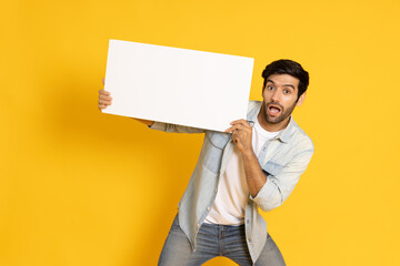 Young man is holding white blank banner or empty copy space advertisement board on yellow...