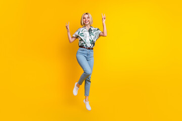Fototapeta na wymiar Full length photo of good mood adorable girl dressed print shirt jumping showing v-sign symbol isolated on yellow color background
