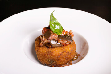 Frittatina di pasta con le melanzane fritta e guarnita con melanzane a funghetto e basilico fresco servita in un pub come antipasto