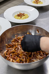 Chef di un ristorante da cerimonia mentre guarnisce un piatto di pasta con della pancetta croccante