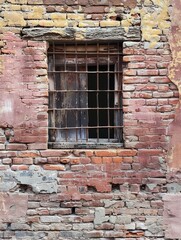 Fototapeta na wymiar An old barred window sits in a dilapidated brick wall, layers of history peeling away. The stark contrast of the window's dark interior with the wall's textured red hues tells a story of time