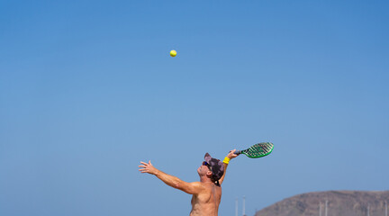 Mature man doing a beach tennis serve