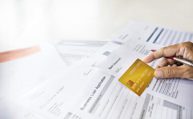 Close-up shot, hand of businessman holding credit card checking bank statement to apply for a loan...