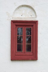Red wood framed window on old weathered white stone wall.