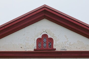 Red wood framed attic window on old weathered white stone wall.