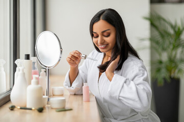 Beautiful millennial indian woman using hair oil
