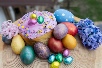 Fototapeta premium multi-colored Easter eggs, homemade Easter cake decorated with chocolate eggs in foil and a large hyacinth flower. Easter concept. Christ is risen. Orthodox holiday