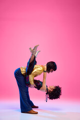 Echoes of 70s. Dance duo, female and male dancers posing in vivid retro fashion outfits against gradient pink studio background. Concept of American culture, 1970s, 1980s fashion, music, art, hobby.