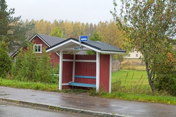 Fototapeta na wymiar Red wood bus stop shelter in countryside in cloudy autumn weather.