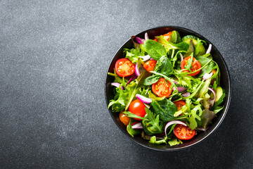 Salad in black bowl at dark background.