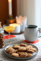 Cup of tea or coffee, stack of books, e-reader, glasses, various cookies, almonds, orange juice and lit candles on the table. Hygge at home. Selective focus.