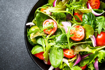 Salad in black bowl at dark background.