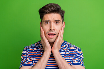 Photo of speechless unsatisfied man arms touch cheeks open mouth cant believe isolated on green color background