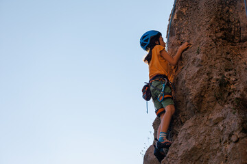 Children's rock climbing. A boy climbs a rock against the backdrop of mountains. Extreme hobby....