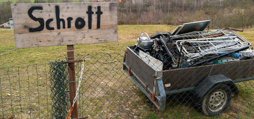wooden sign with the word scrap in German and a trailer with scrap metal