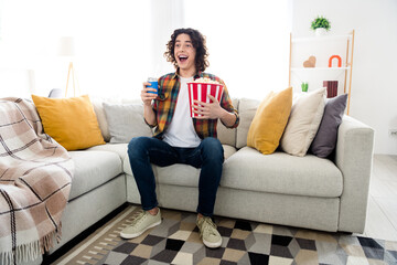 Full length photo of impressed funny guy dressed checkered shirt watching film eating popcorn drinking cola indoors house home room - obrazy, fototapety, plakaty