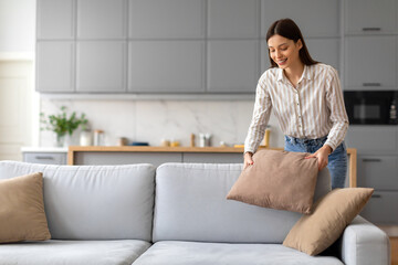 Smiling young woman arranging cushions on sofa