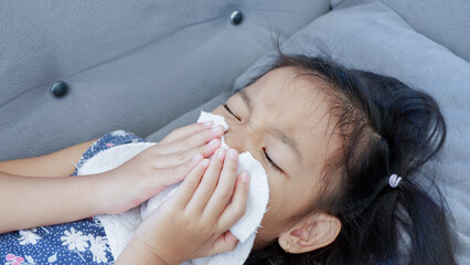Girl blowing nose with tissue or white napkin at home.