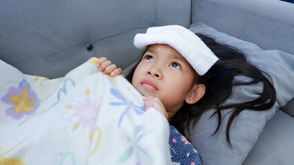 Asian child girl fever on couch with white towel on forehead. Kids healthcare concept