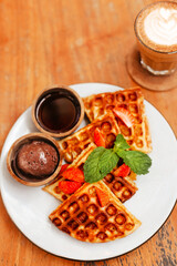 Waffles with berries and toppings on a white plate. Appetizing waffles with chocolate and coffee. Concept of delicious breakfasts in a hotel