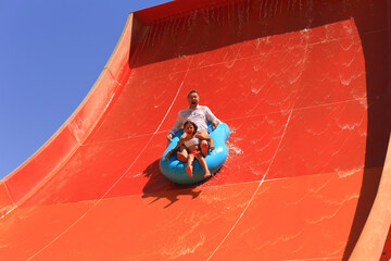 Family going down a water slide at a water park in summer. Father and little daughter ride on...