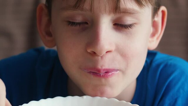 portrait of a happy Caucasian boy 9 years old eating cornflakes with milk with a spoon from a plate looking at the camera. morning breakfast for a child made from milk and cereals