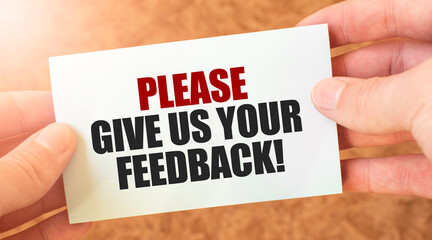 PLEASE GIVE US YOUR FEEDBACK word inscription on white card paper sheet in hands of a businessman.