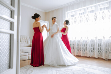 Bridesmaids rejoice in the morning, helping to fasten the buttons on the wedding dress and prepare for the wedding ceremony. They take pictures, smile, help the bride with her shoes.