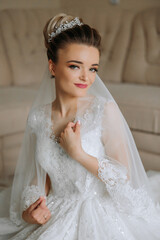 fashion photo of a beautiful bride with dark hair in an elegant wedding dress and stunning makeup in the room on the morning of the wedding. The bride is preparing for the wedding