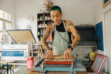 Female worker with squeegee is printing images on textile by silkscreen method in a design studio