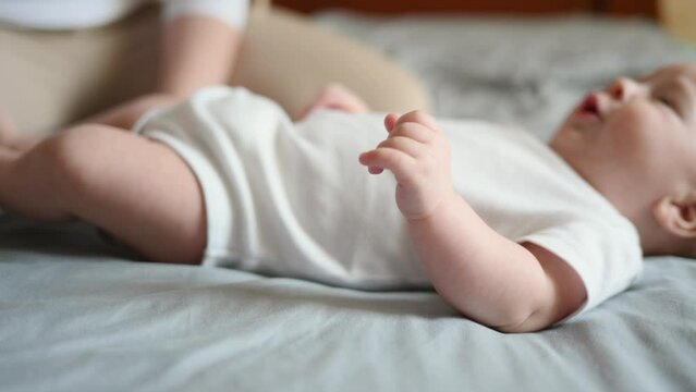 Newborn baby lying in bed in light clothes, hearing his mother, shows activity, kicking his legs and arms. Happy childhood. Carefree healthy childhood, infancy. Soft focus