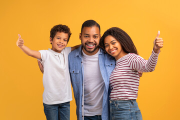 Cheerful black family with preteen son giving thumbs up at camera