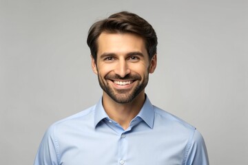 Obraz premium A charming young man wearing a white shirt stands against a grey background, smiling and confidently gazing at the camera.