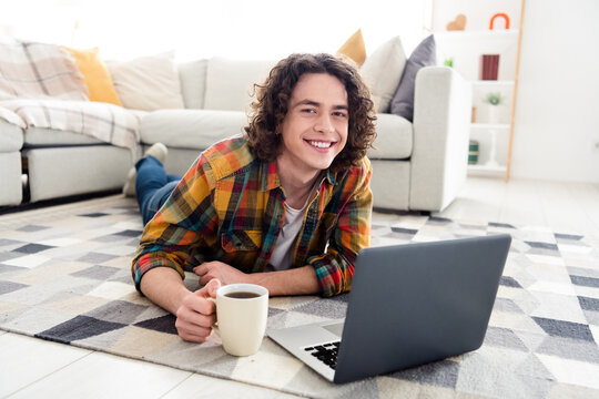 Photo of positive charming guy dressed checkered shirt enjoying beverage reading modern device indoors house home room