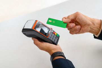 Focused on a green credit card being tapped on a contactless payment device held by a person