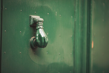 Old door knocker of historical building clode up. Doorknob in a shape of woman hand, on a green...