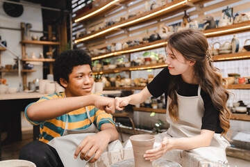 Two multi-ethnic friend is enjoy a having fun while learning a pottery or sculpture workshop,...