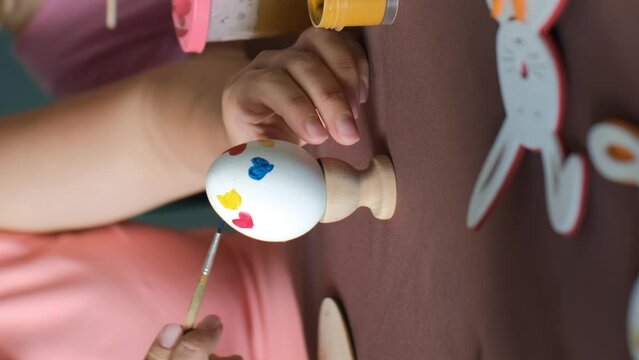 Vertical video. Close-up of mother with daughter painting eggs for Easter together in the kitchen