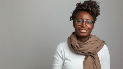 Obraz premium a smiling person is wearing round eyeglasses and a scarf, giving off a relaxed and stylish vibe against a gray background.
