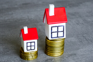 Two different sizes tiny houses on two different height stacks of coins symbolizing different costs