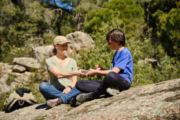 Mother and son sitting on a rock with a stainless steel lunch box in the forest.